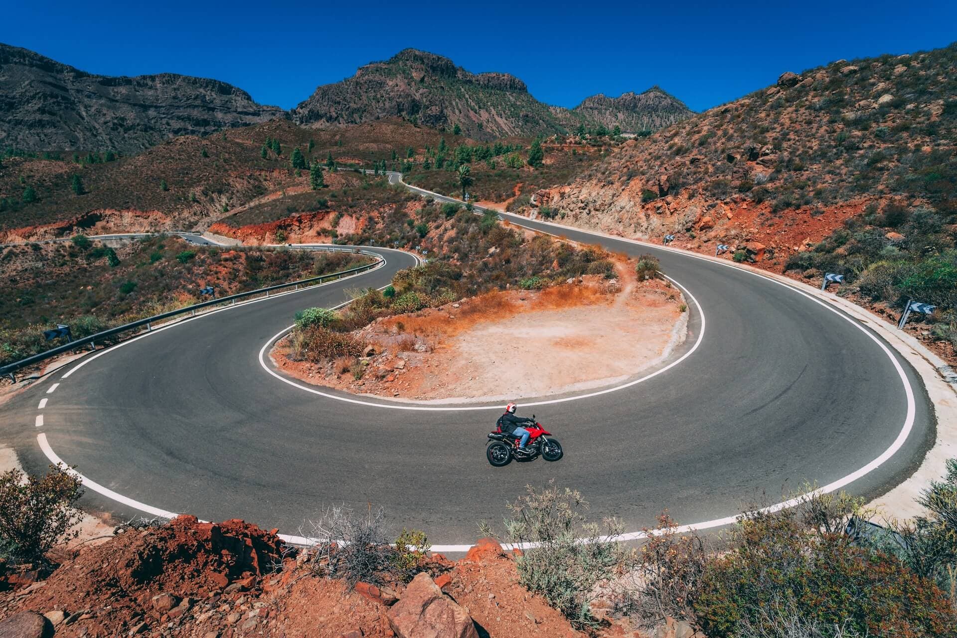 Motorcyclist leaning through a horseshoe hairpin bend on a volcanic mountain road in Gran Canaria